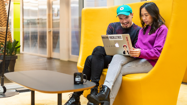 Two colleagues sitting on a sofa looking at a laptop in a trendy office