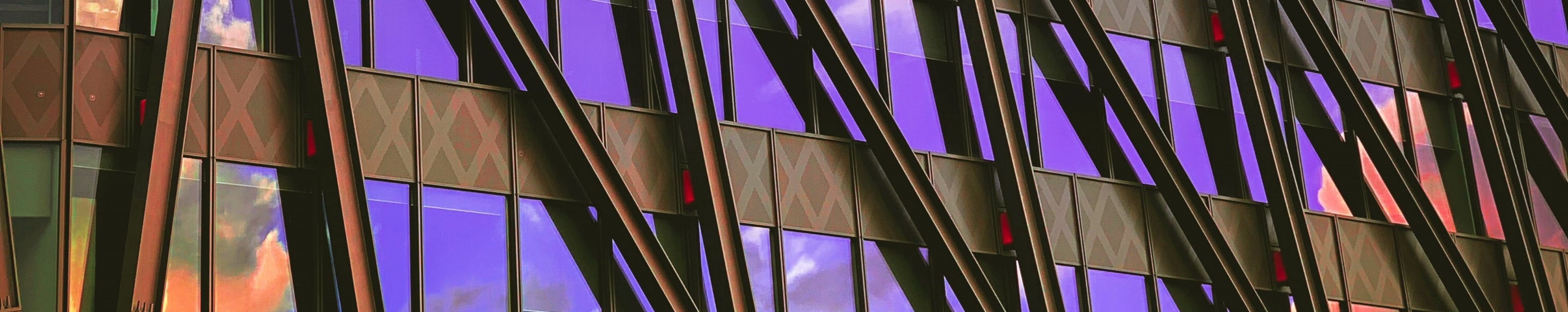 Glass windows of a building reflecting the purple sky and orange clouds.