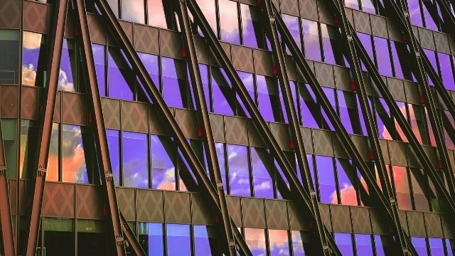 Glass windows of a building reflecting the purple sky and orange clouds.