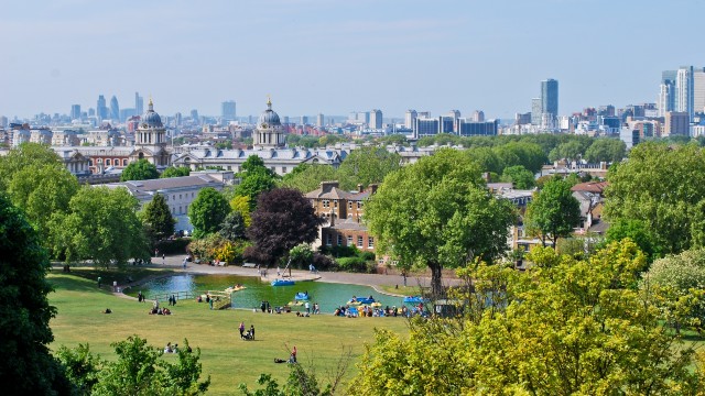The city skyline in the distance from a hill in one of London's parks. Trees and a water body are in the centre shot. 