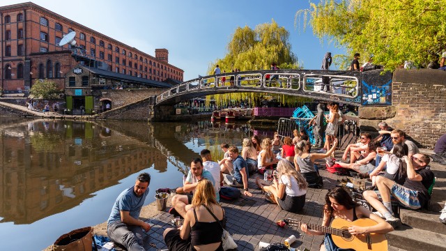 People sat beside Regent's Canal, dressed in summer clothes on a bright day.