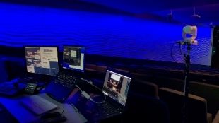 Studio set up at the Barbican, showing three monitors and a camera in front of a dark blue light backdrop.