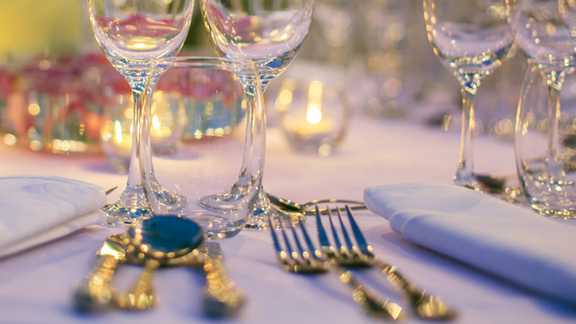 Dinner table close-up, with wine glasses, cutlery and candle lights placed in an elegant setting.