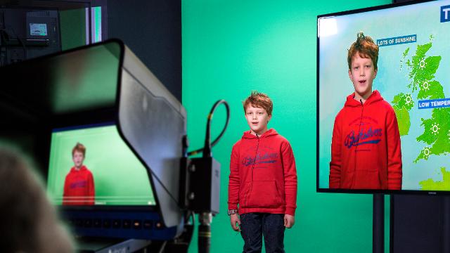A young boy stood in front of a green screen, pretending to be a weatherman