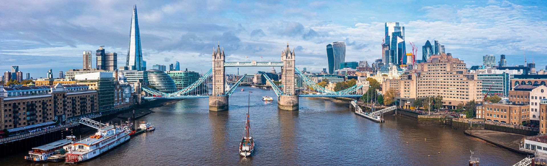 An aerial view of Tower Bridge with a boat passing through on the river Thames, and The Shard and City of London in the distance 