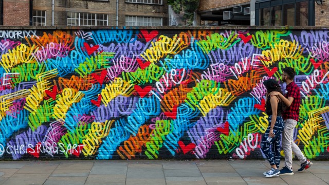 Two people walking in front of a wall of street art in east London. 