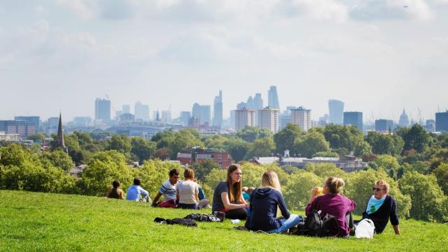 People enjoy the sunshine on Primrose Hill in London with the city of London in the distance