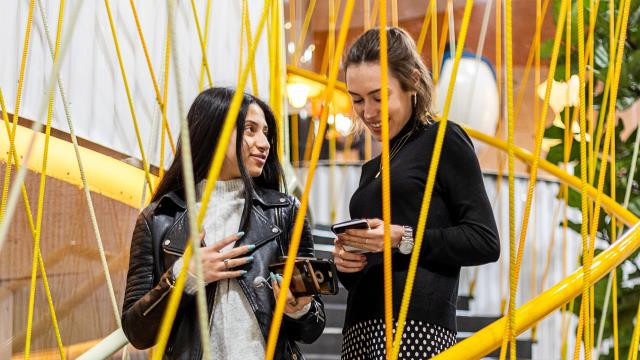 Two people share a joke on a staircase wrapped with yellow steel rods at Second Home in Spitalfields