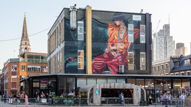A large mural of a fashionable woman on the side of a building, above a bar, in Spitalfields.