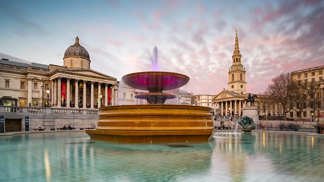 The sun is rising on the fountain of Trafalgar Square.