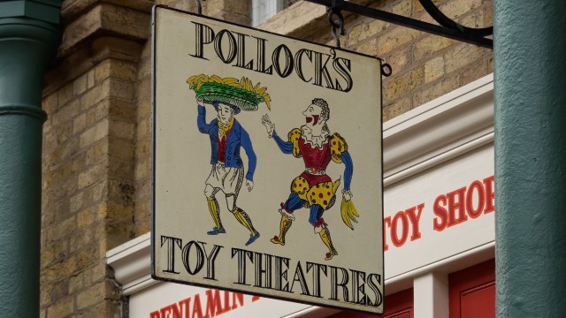 The Benjamin Pollock's Toyshop sign which reads Pollock's Toy Theatre and has an animated jester reaching out to an animated man carrying a large plate of bananas on his head.
