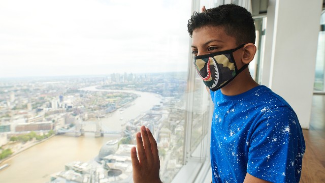 A young boy wearing a face covering looks out over the London skyline from The View from The Shard. 