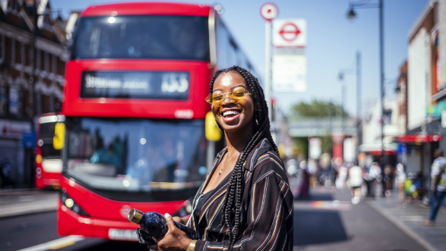 A smiling girl waits for a bus at a bus stop on sunny summer's day in London.