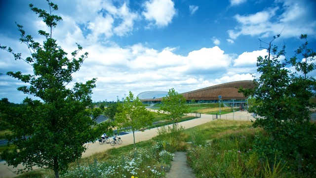 Views over the Lee Valley VeloPark and surrounding green space as cyclists ride along the path outside the velodrome 