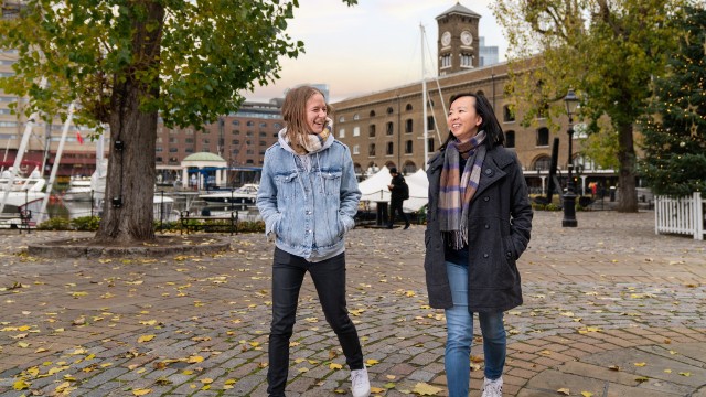 Two people smile while walking along the cobbled pathways of St Katharine Docks. 
