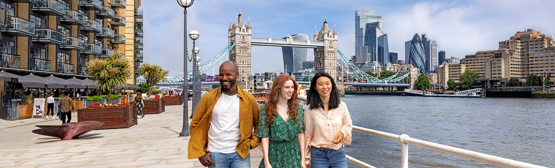 Man and two women walking alongside the river Thames with Tower Bridge and the City of London in the background