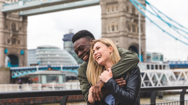 A couple laugh as they explore London with Tower Bridge in the background. 