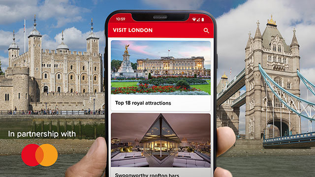 An image of a mobile phone showing the Visit London app, featuring the Mastercard log.  the Tower of London, and Tower Bridge in the background on a sunny day