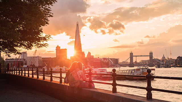 Two girls standing on the South Bank by the river Thames at sunset with The Shard and Tower Bridge in the background.