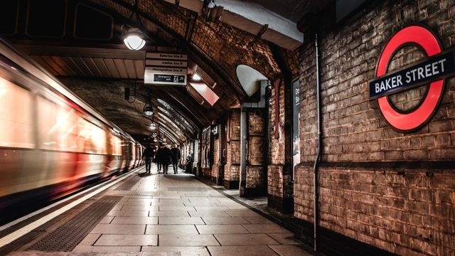 A train travels through the baker street london underground station where people are walking on the platform. 