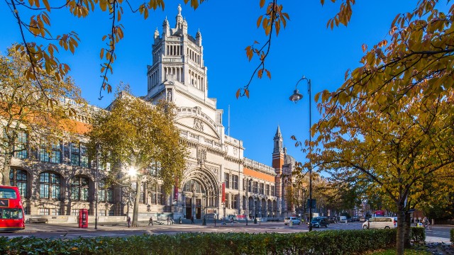 A view of the exterior of the Victoria and Albert Museum with autumnal trees in the forefront