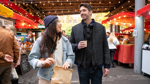 A woman and a man walk through Borough Market in London surrounded by colourful food stalls.