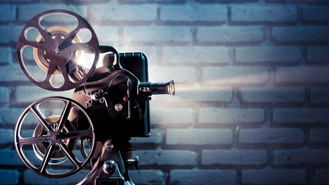 Film projector emitting a beam of light located against a brick wall.