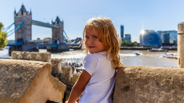 Young blonde girl posing in front of Tower Bridge and the river Thames on a summer's day.