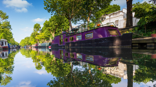 Purple canal boat moored in London's Little Venice canal lined with trees.