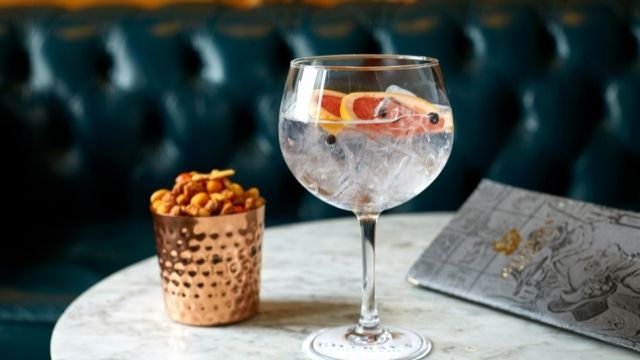 A glass of gin with pomegranate sits on a table with a side of nuts and bar menu.  © Richard Fairclough 