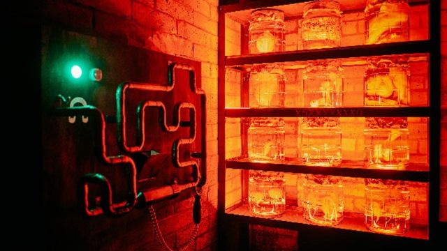 An orange escape room with a shelf of jars filled with mysterious ingredients and pipes on the adjacent wall. 