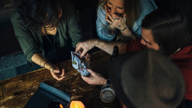 A group of people sit at a brown table holding clues to an escape room.