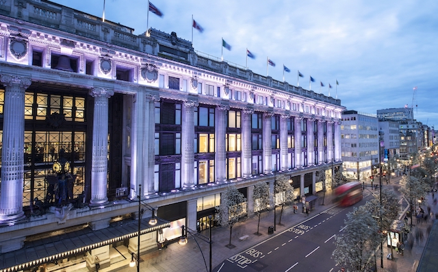 Illuminated exterior of Selfridges department store on Oxford Street in London at dusk.