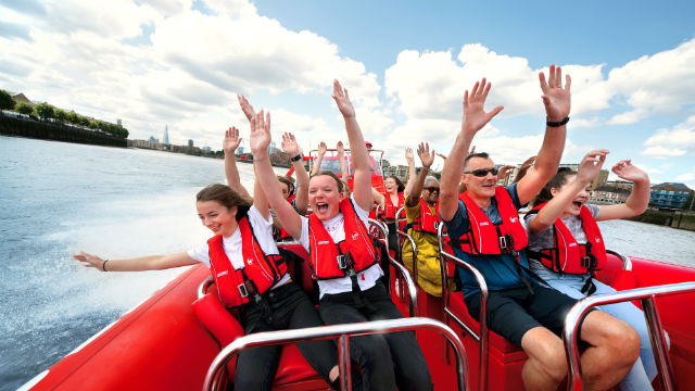 People enjoying a boat ride, with their hands up in the air on a bright day.