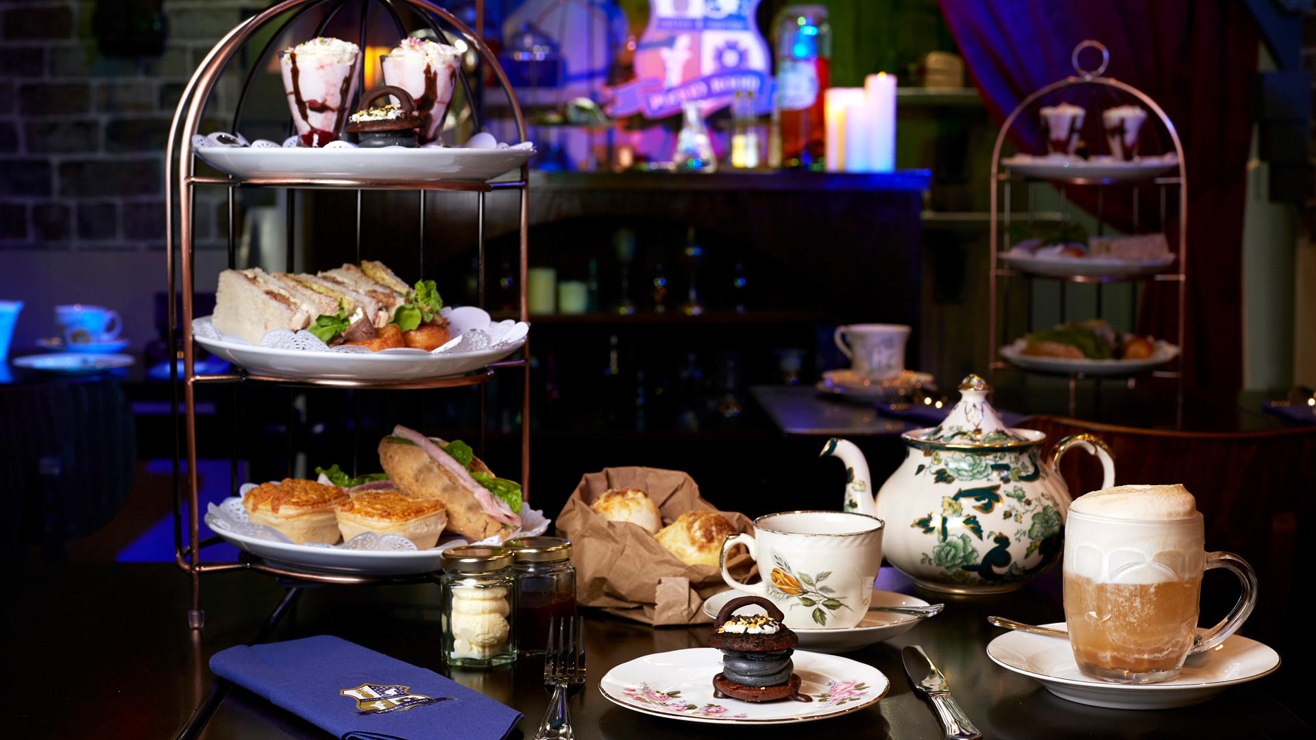 Afternoon tea at the Potion Room. Image courtesy of Cutter & Squidge. An afternoon tea spread for wizards, including a stand filled with cakes, finger sandwiches and treats, with a teapot, scones and plates laid out on the table.