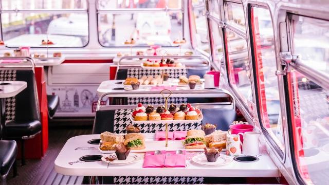 The top deck of a routemaster bus, with plates and tiered cake stands full of sandwiches and cakes.