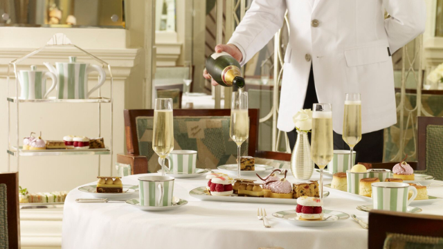 Waiter pouring champagne into flutes accompanying afternoon tea scones and sandwiches. 