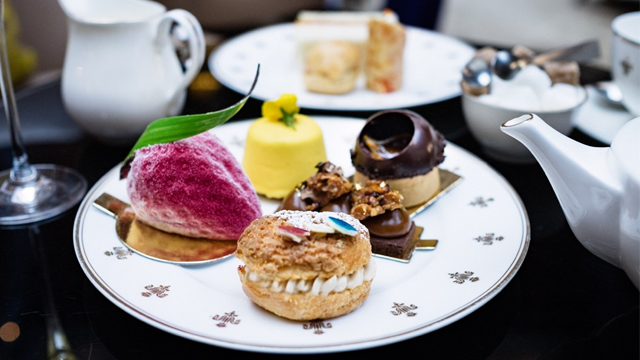 Mini patisseries including a strawberry cake, a lemon dessert, a chocolate treat and a Paris-Brest on a white plate alongside a pot of tea and a pot of milk.