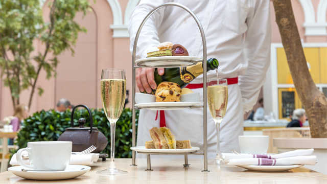 Afternoon tea treats on a three-tiered tray alongside glasses of champagne and a pot of tea.