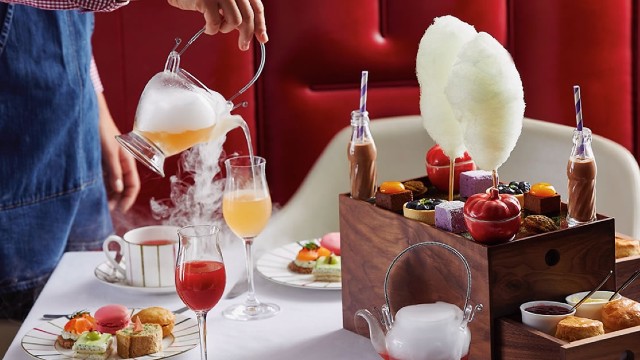 A person pouring tea into a glass, with afternoon tea nibbles displayed on a table around.