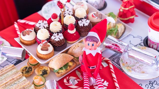 Festive cakes and savoury treats line a table covered in christmas decorations and a small elf toy aboard a Brigit’s Bakery tour bus. 