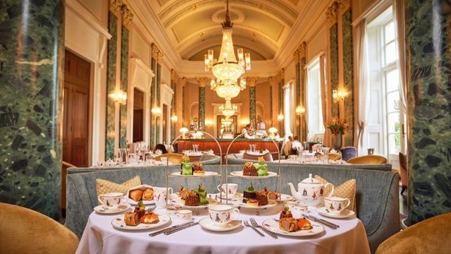 Tables with plush sofas and chairs and christmas afternoon tea treats sit in an opulent room with pillars and chandeliers at the theatre royal drury lane.