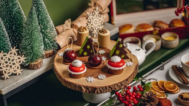 Small green christmas trees, dried orange slices and scones surround a wooden table with christmas themed afternoon tea treats.