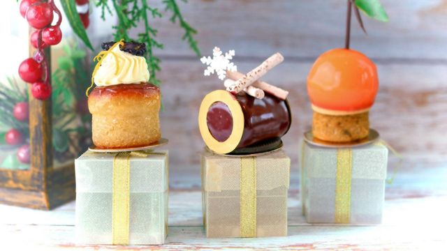 Three christmas pastries, one cake, one chocolate yule log and one orange sweet treat, sit atop mini presents at the intercontinental O2 afternoon tea.