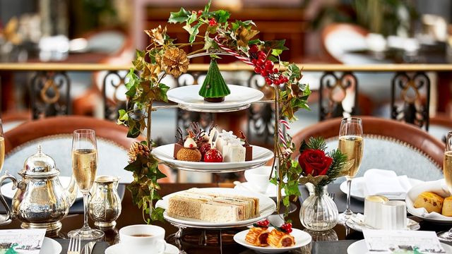 Ein gedeckter Tisch mit einem weihnachtlichen Nachmittagstee, mit Stechpalmen geschmückten Tellern und süßen Leckereien sowie Weihnachtscocktails.