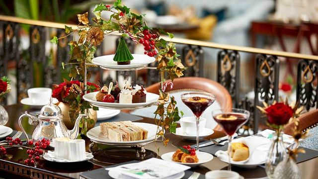 An indulgent table covered in a Christmas-themed afternoon tea with plates adorned with Holly and sweet treats with Christmas cocktails.