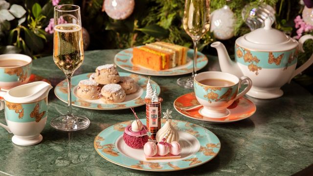Christmas-themed pink treats are laid out of decorative plates with champagne and a pot of tea.