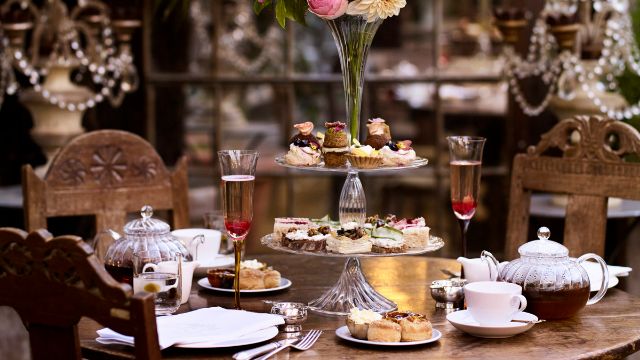 A table laid out with beautiful crockery in a rustic restaurant with a delightful afternoon tea spread of cakes and sandwiches. 