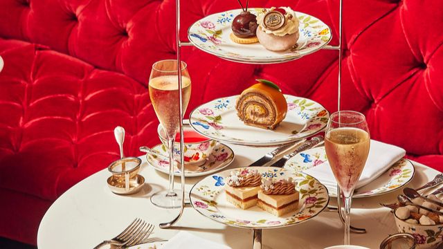 A table with a white tablecloth covered in a festive afternoon tea spread against a bright red velvet sofa.