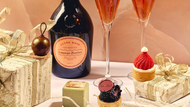 A selection of festive sweet treats sit atop golden presents next to a bottle of rose champagne. 